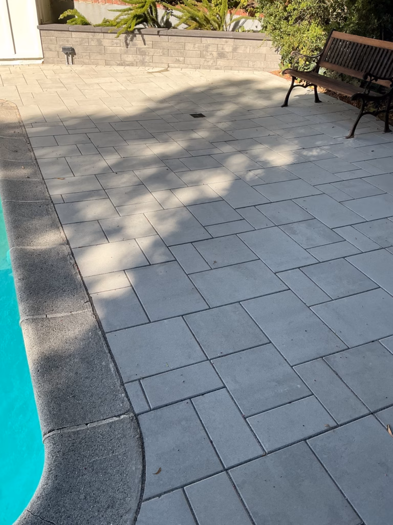 Rounded pool coping and light gray pavers, with a garden bench and the new Melville wall beyond