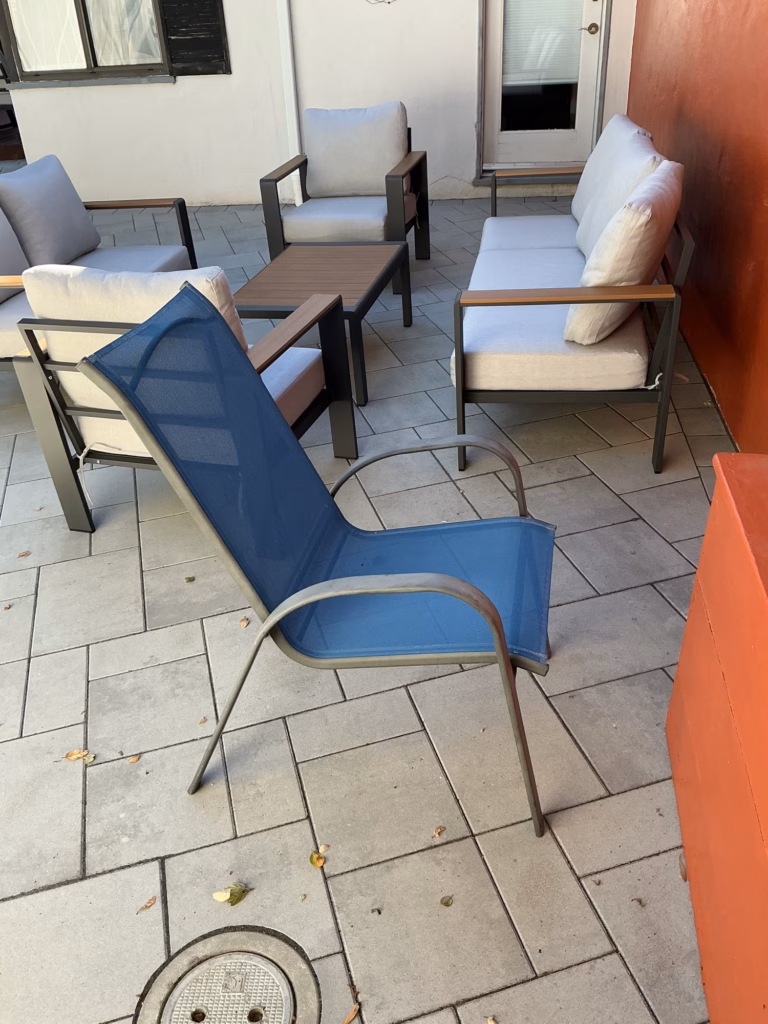 Outdoor chairs and a sofa on light gray pavers beside an orange wall and a door