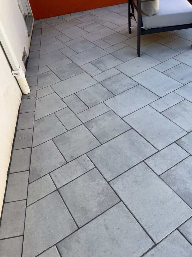 Three-piece paver pattern along a white stucco wall, with the corner of a sofa at the edge of the frame