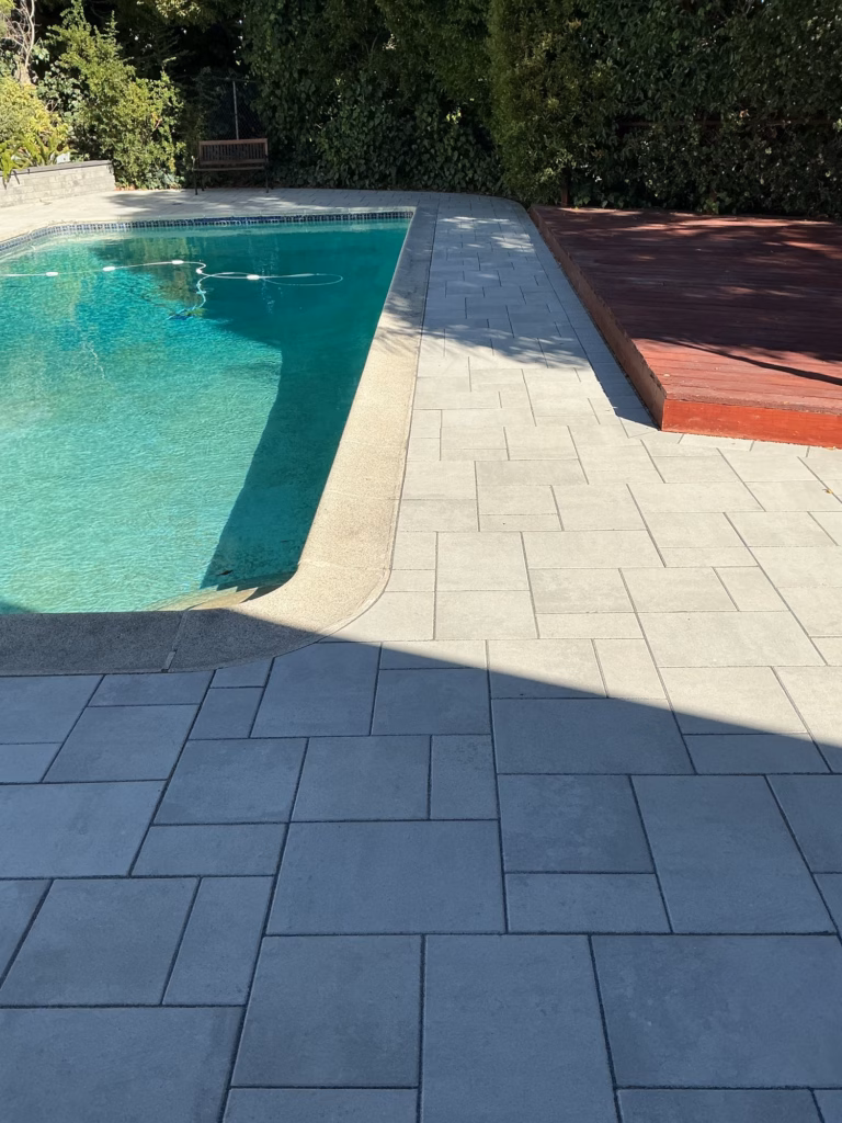 Light gray Belgard pavers around a pool, beside a red-stained wood deck and a tall hedge in a Hillsborough backyard