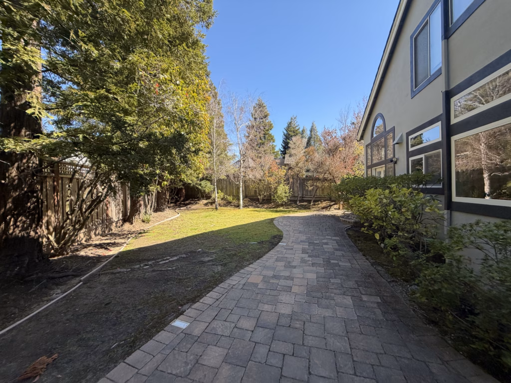 Before — curving older paver path between a lawn and the back of a two-story San Mateo house