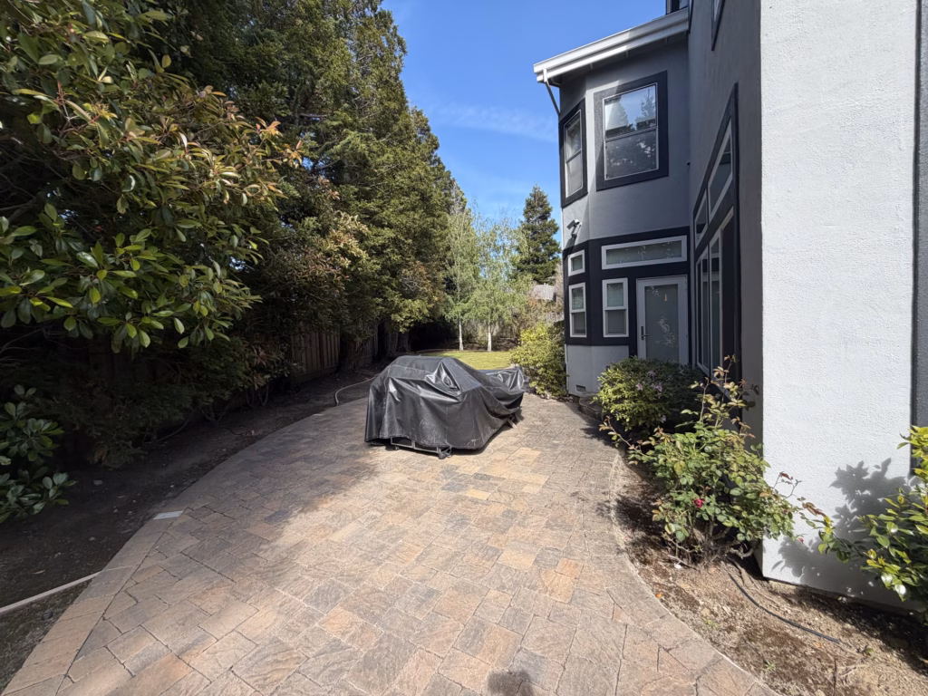 Before — older paver patio with a covered grill beside a bay window and side door